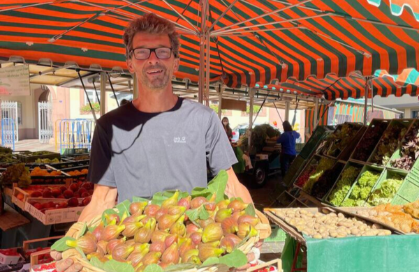 Bild vergr&ouml;&szlig;ern: Martin Braun an seinem Obst- und Gemüsestand auf dem Neustadter Marktplatz. Er trägt einen großen Korb mit frischen Feigen.