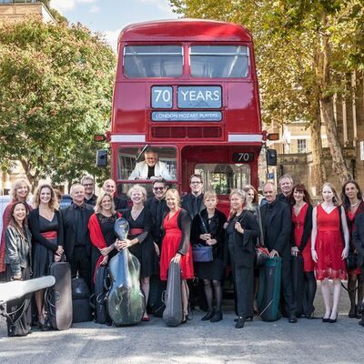 Die Musiker des Orchesters London Mozart Players stehen mit ihren Instrumenten vor einem roten Doppeldeckerbus.