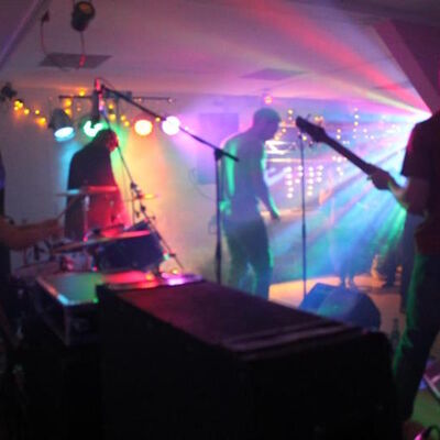 Blick in einen Raum mit einer spielenden Band und buntem Scheinwerferlicht.