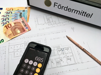 Bild vergr&ouml;&szlig;ern: Ein Ordner mit der Aufschrift "Fördermittel" liegt auf Planungsunterlagen. Daneben Geldscheine und ein Handy mit der Taschenrechnerfunktion. Das Bild verlinkt zu weiteren Informationen über die KIPKI-Bürgerförderung der Stadt Neustadt an der Weinstraße.