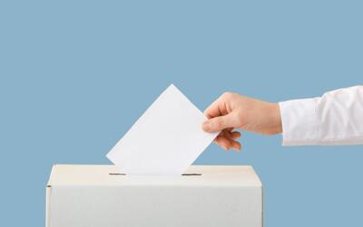 Bild vergr&ouml;&szlig;ern: Auf dem Bild steckt eine Hand einen Zettel in einen Wahlzettelkasten.