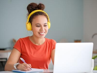 Bild vergr&ouml;&szlig;ern: Junge Frau mit gelben Kopfhörern nimmt an einem Onlinekurs am Laptop teil.