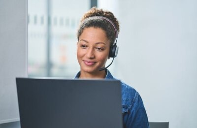 Bild vergr&ouml;&szlig;ern: Eine Frau sitzt mit Headset an einem Laptop