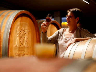 Eine Frau verkostet in einem Weinkeller vor einem Holzfass einen Rotwein