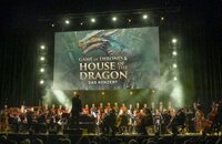 Bild vergr&ouml;&szlig;ern: Ein Orchester spielt auf der Bühne die Musik von Games of Thrones und House of Dragons. Im Hintergrund ein Plakat mit einem Drachen.