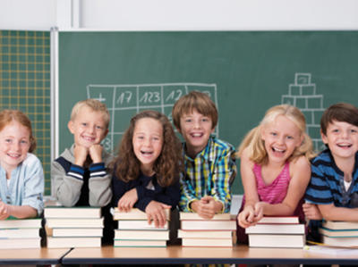 Bild vergrößern: Schulkinder mit Büchern vor einer Schultafel
