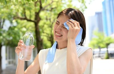 Bild vergr&ouml;&szlig;ern: Eine Frau hat eine Wasserflasche in der Hand und wischt sich den Schweiß von der Stirn