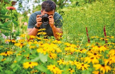 Bild vergr&ouml;&szlig;ern: Ein Mann fotografiert gelbe Blumen in einem Garten