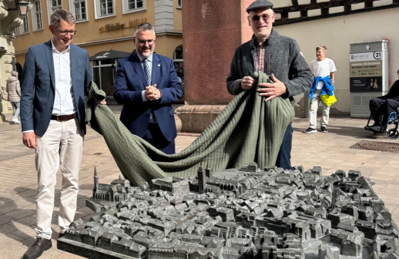 Bild vergr&ouml;&szlig;ern: Enthüllen das neue Stadtrelief, das auch über Erklärungen in Blindenschrift verfügt (v.li.): Baudezernent Bernhard Adams, OB Marc Weigel und Peter Reinhardt von der Bürgerstiftung.
