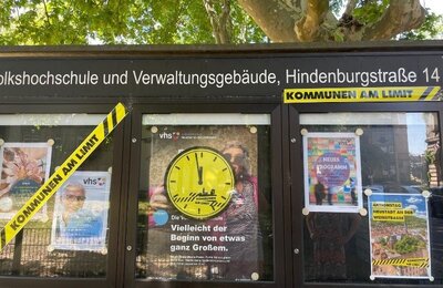 Bild vergrößern: Ein mit Absperrbändern und Plakaten ausstaffierter Schaukasten der Volkshochschule Neustadt an der Weinstraße am Aktionstag "Kommunen am Limit" am 22.06.2026.