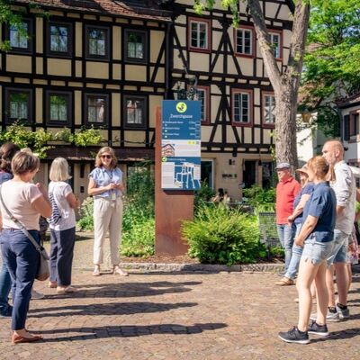 Bild vergr&ouml;&szlig;ern: Eine Gruppe von Menschen bei einer Stadtführung mit Fachwerkhäusern im Hintergrund