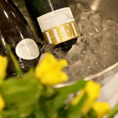 Bild vergr&ouml;&szlig;ern: Flaschen Sekt in einem Kühlbehälter auf Eis mit gelben Blumen im Vordergrund - Sektprobe und Kellerführung